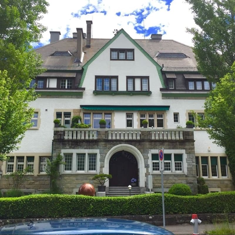 2 story house, white exterior, brown roof, balcony, multiple windows, front door, garden, trees