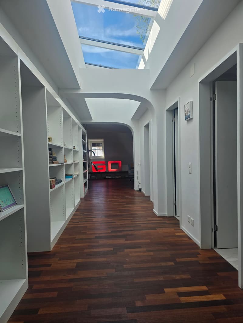 Bright, modern hallway with wooden flooring, white walls, built-in shelving on one side, and a skylight at the top.