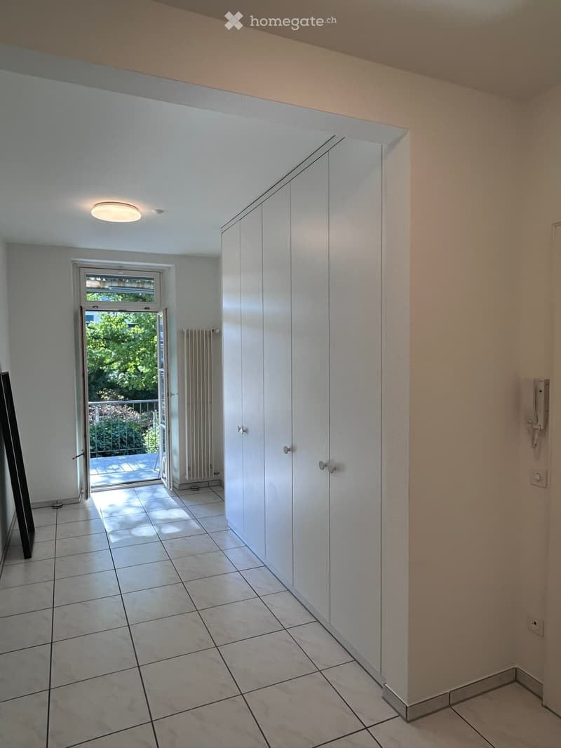 Empty hallway with white walls, tiled floor, built-in white closet, and a sliding glass door leading to a balcony area.