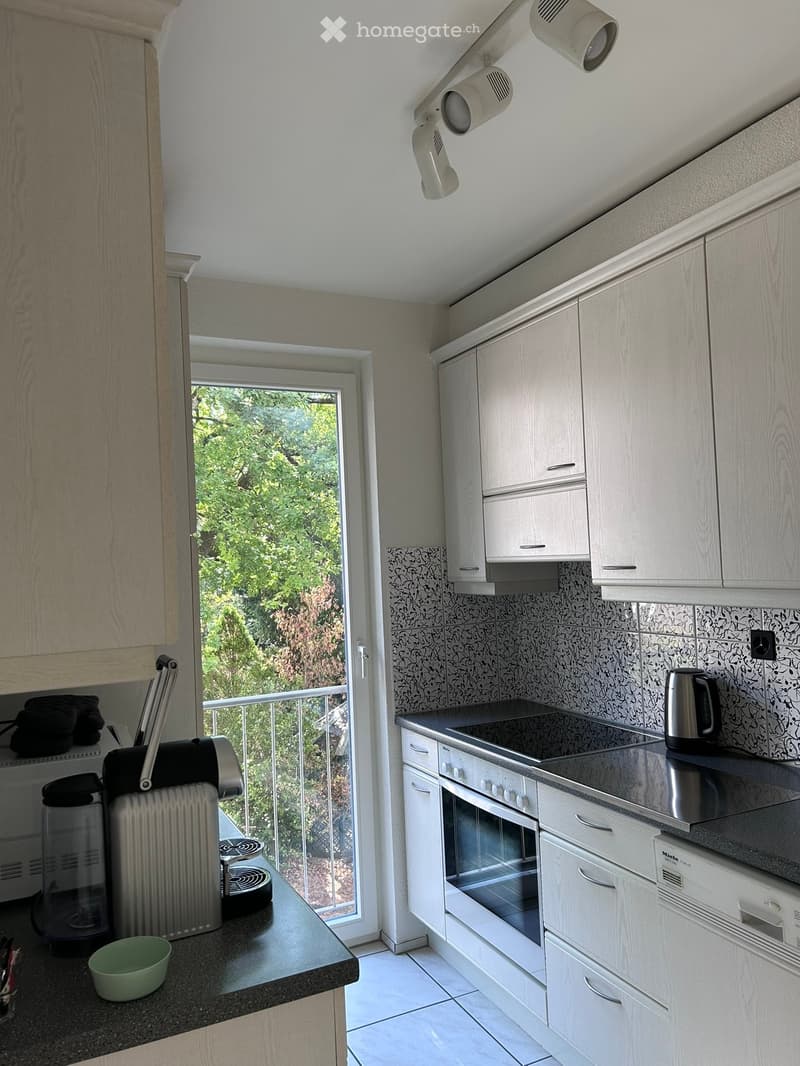 Modern kitchen with white cabinets, stainless steel appliances, and a black countertop. Features an oven, stove, coffee maker, and a cup on the counter.