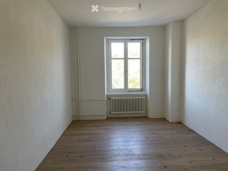Empty room with wooden flooring, white walls, a single window, and a radiator below it. No furniture or equipment present.