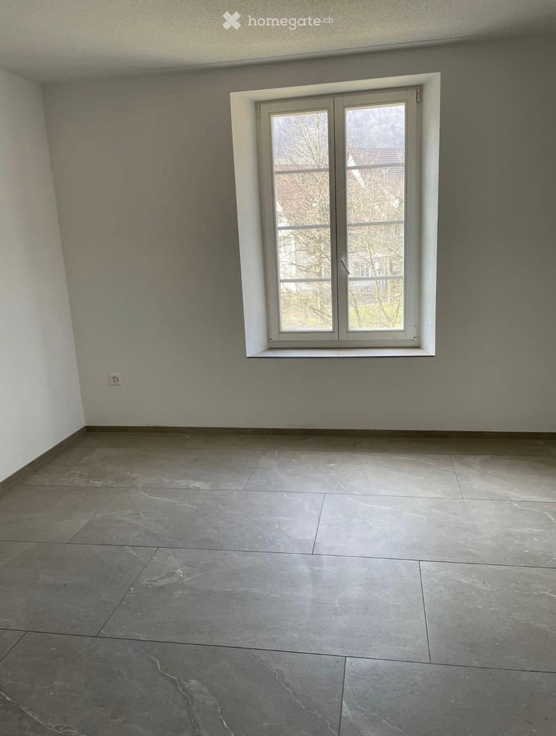 Empty room with grey tiled floor and white walls, featuring a single window with white frame and glass panels.