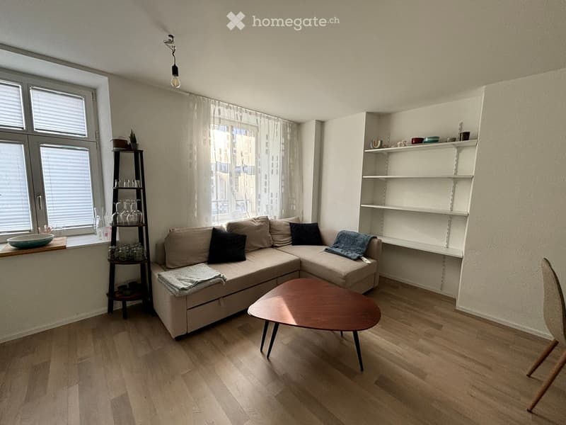 Modern living room with a sectional sofa, coffee table, shelves, and a view of the city through large windows.