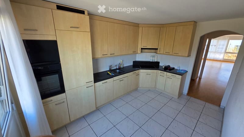 Modern kitchen with light wooden cabinets, white tiled floor, black countertop, and stainless steel sink.