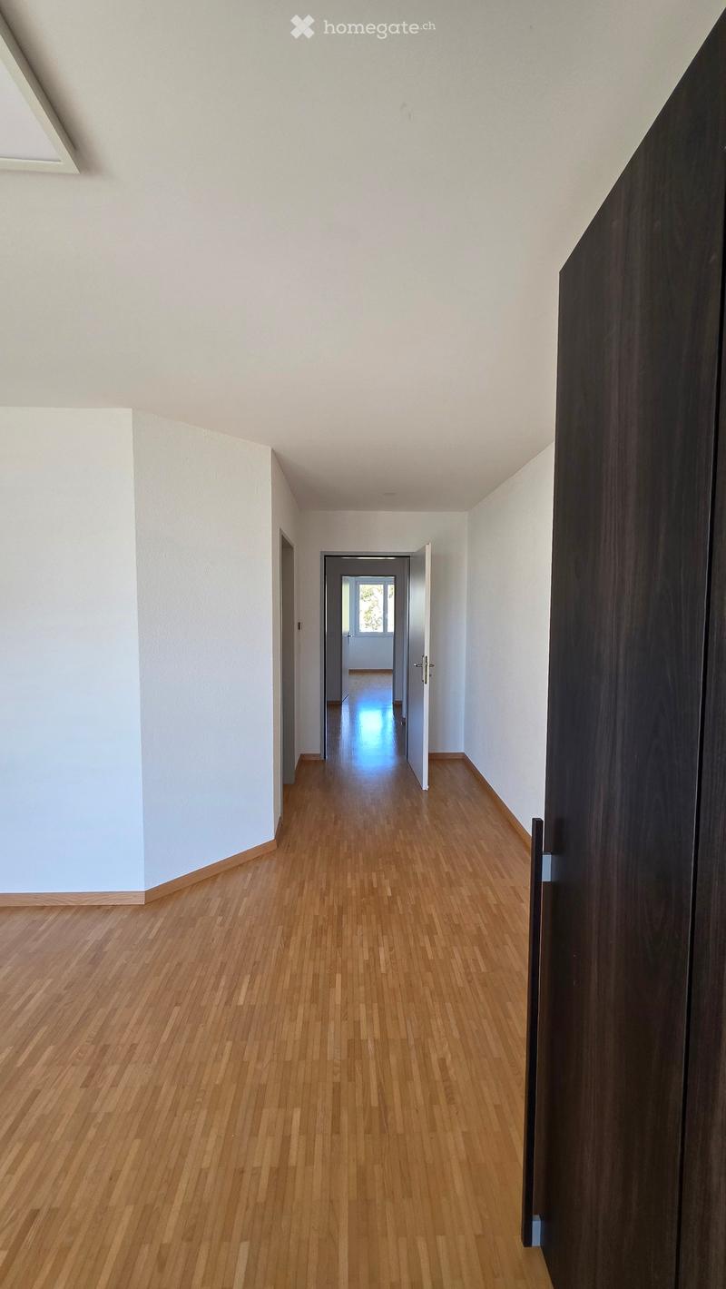 Empty hallway with wooden flooring, white walls, and a partially open door leading to another room.