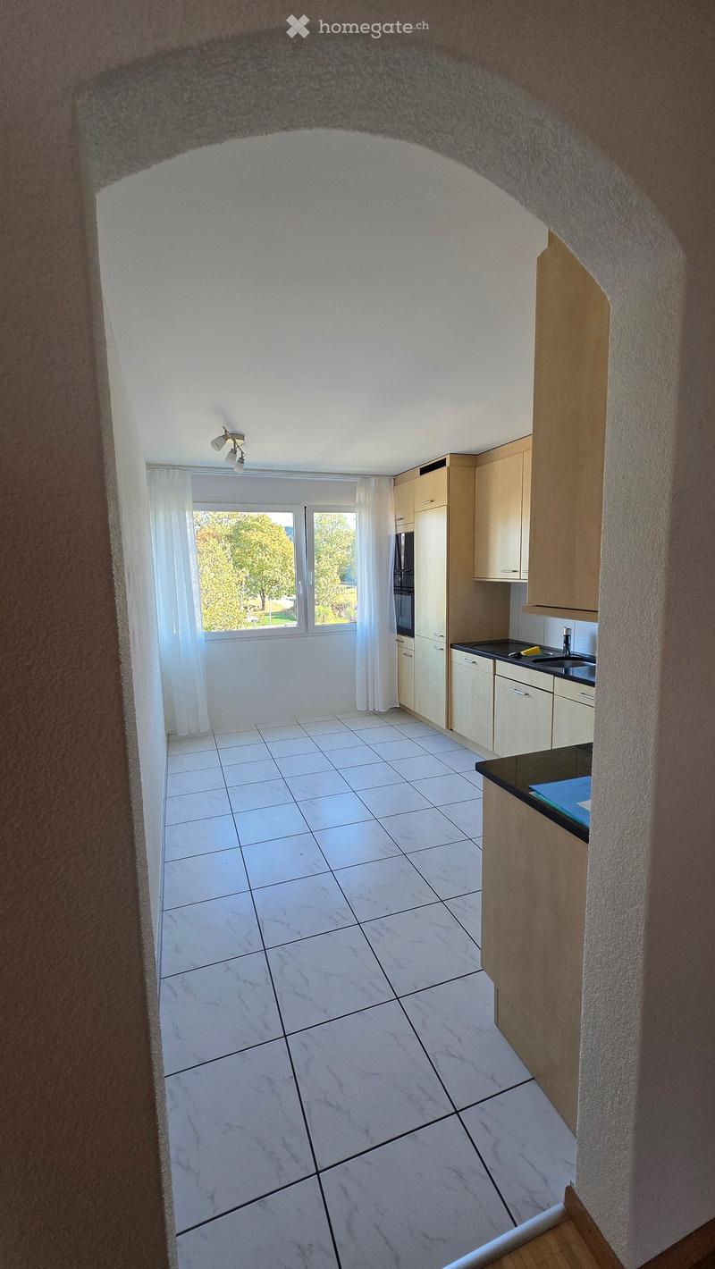 Modern kitchen with white tiled floor, light wooden cabinets, black countertop, and a window with white curtains.