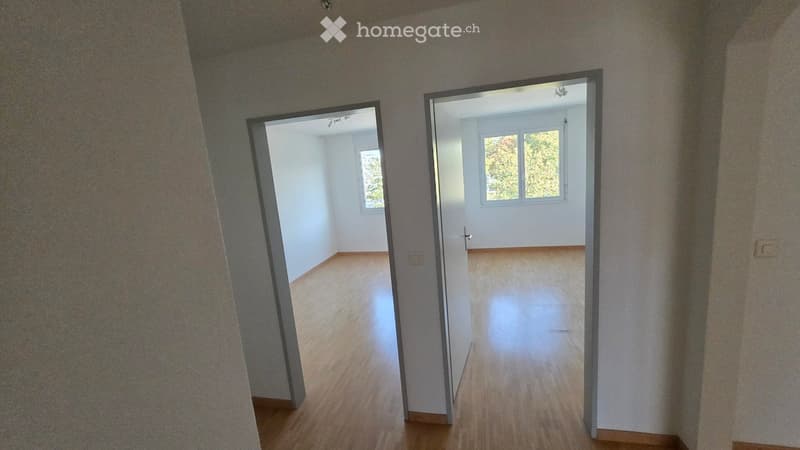 Empty hallway with wooden flooring, two open doors leading to adjacent rooms, and white walls.