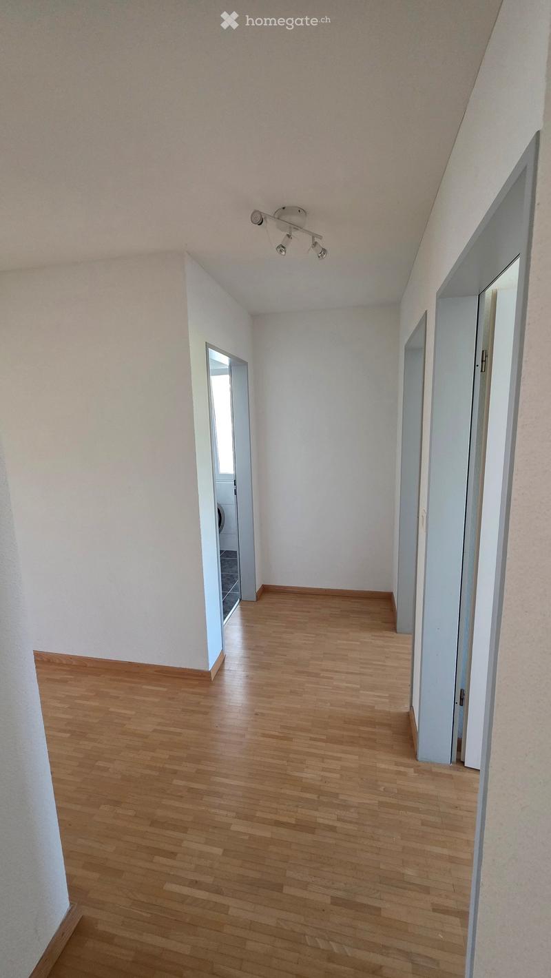 Empty hallway with wooden flooring, white walls, and multiple doors leading to other rooms.