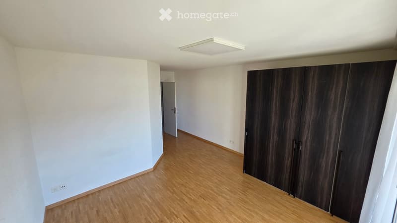 Empty room with light-colored walls, wooden flooring, and a large dark wooden wardrobe. No furniture or personal items are present.