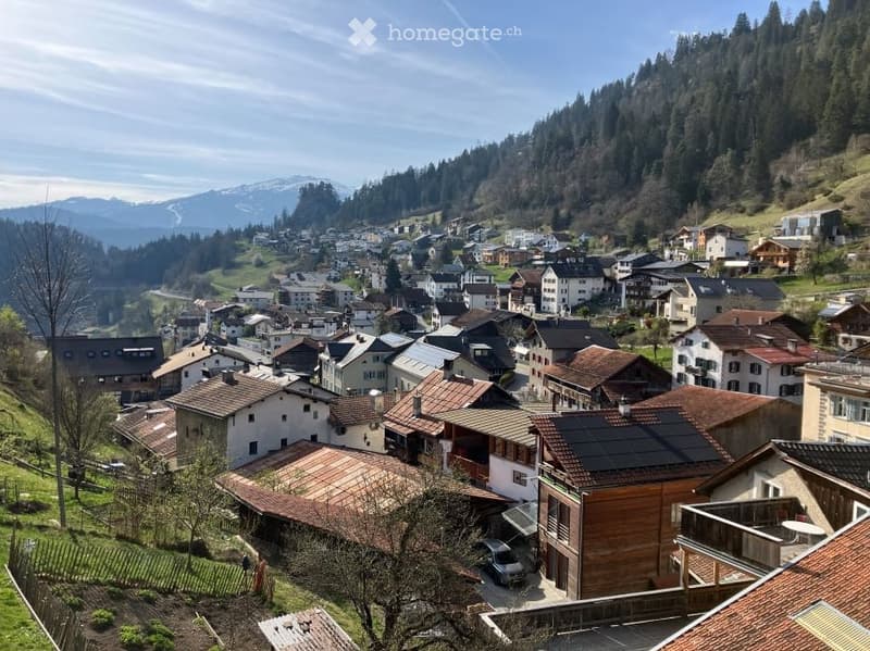 A picturesque village nestled in a valley with traditional houses, red-tiled roofs, and surrounded by lush green hills and mountains.