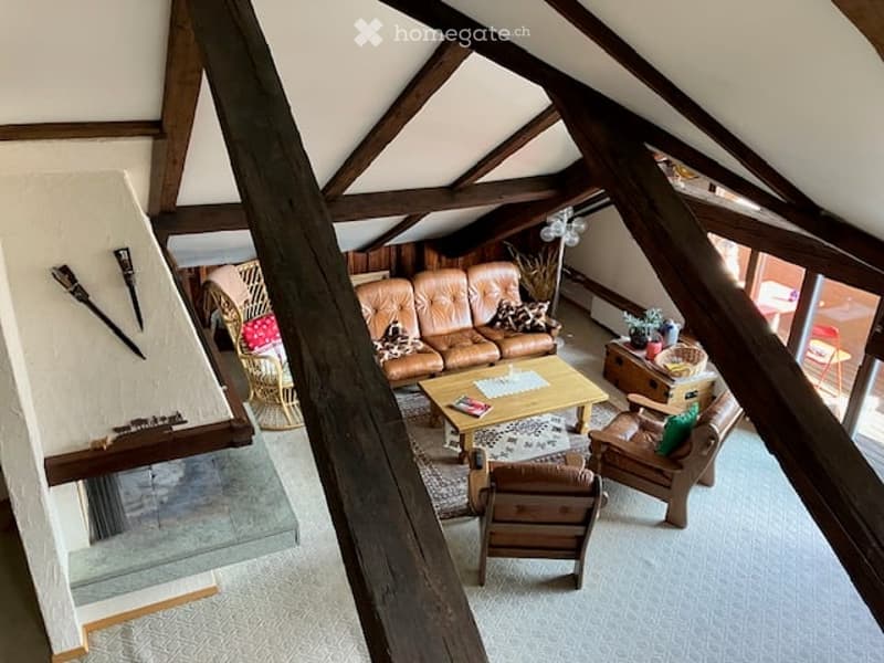 Living room with exposed wooden beams, a brown leather sofa, coffee table, armchairs, and a floor lamp. The room features a mix of wooden and leather furniture, with a cozy and inviting atmosphere.