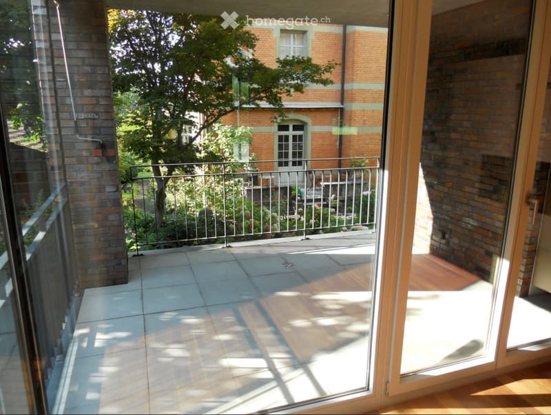 Balcony with tiled floor, metal railing, and view of a garden and brick building.