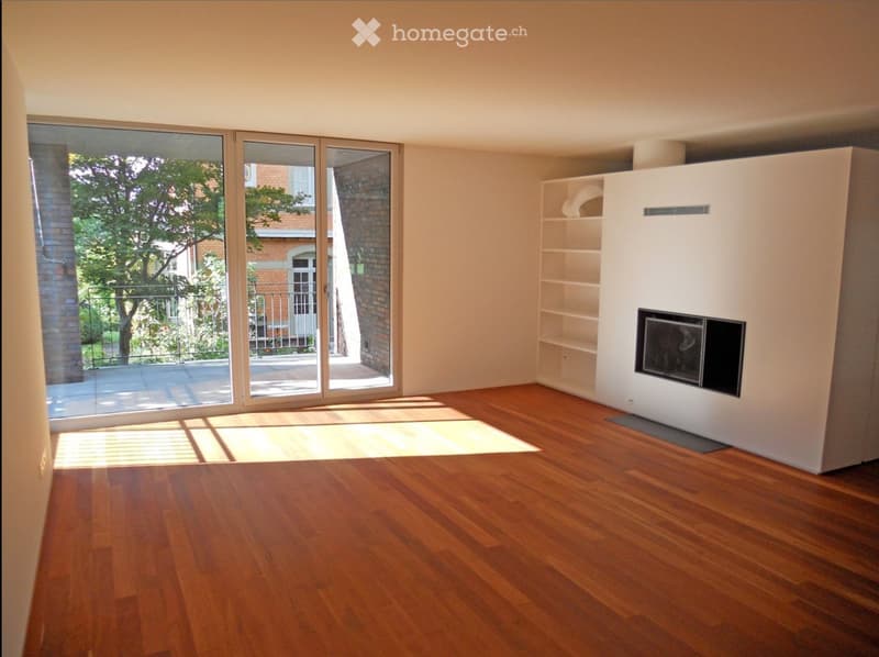 Empty room with wooden flooring, large sliding glass doors leading to a balcony, and a built-in fireplace unit with shelves.