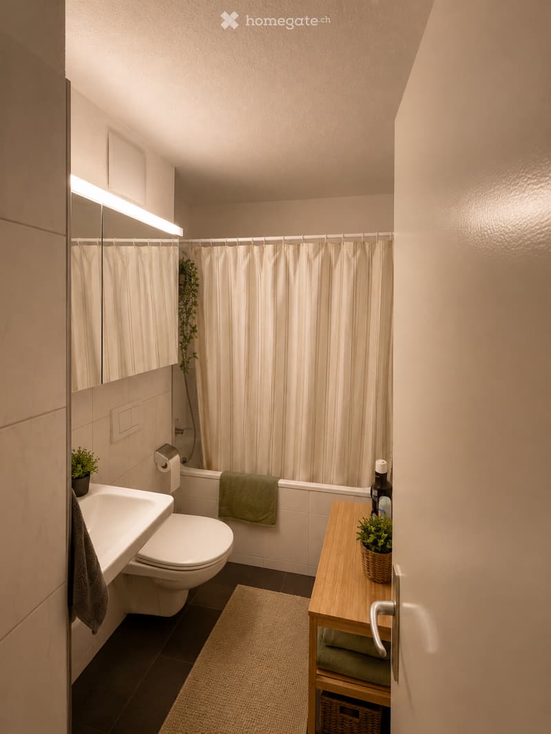 Modern bathroom with a white sink, toilet, bathtub, and a small wooden table with a plant. Features a striped shower curtain, a towel on the edge of the tub, and a small potted plant on the sink counter.