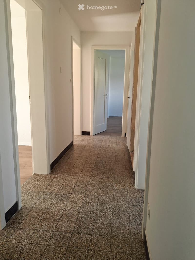 Empty hallway with tiled floor and white walls, featuring several doors and a wooden section on the left side.
