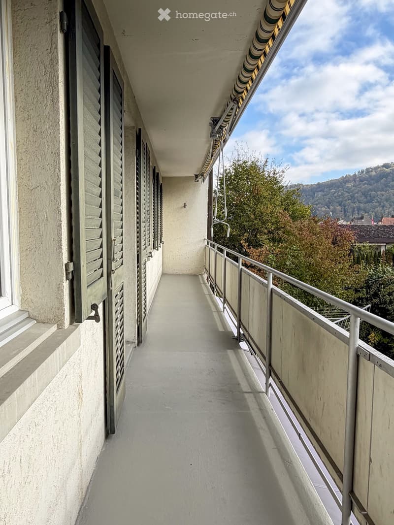 Balcony with metal railing, concrete floor, and scenic view of greenery and hills.