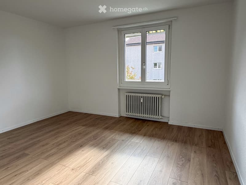 Empty room with wooden flooring, white walls, and a window with a radiator below it.