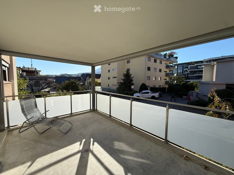 Balcony with a lounge chair, metal railing, and a view of the city and surrounding buildings.