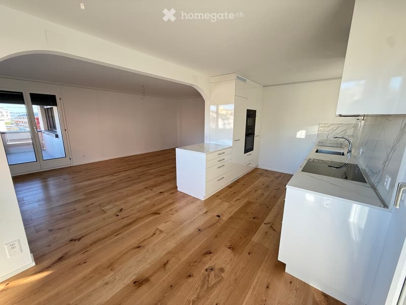 Modern kitchen with white cabinets, marble countertops, and a wooden floor. Features a sink, oven, and ample storage space.