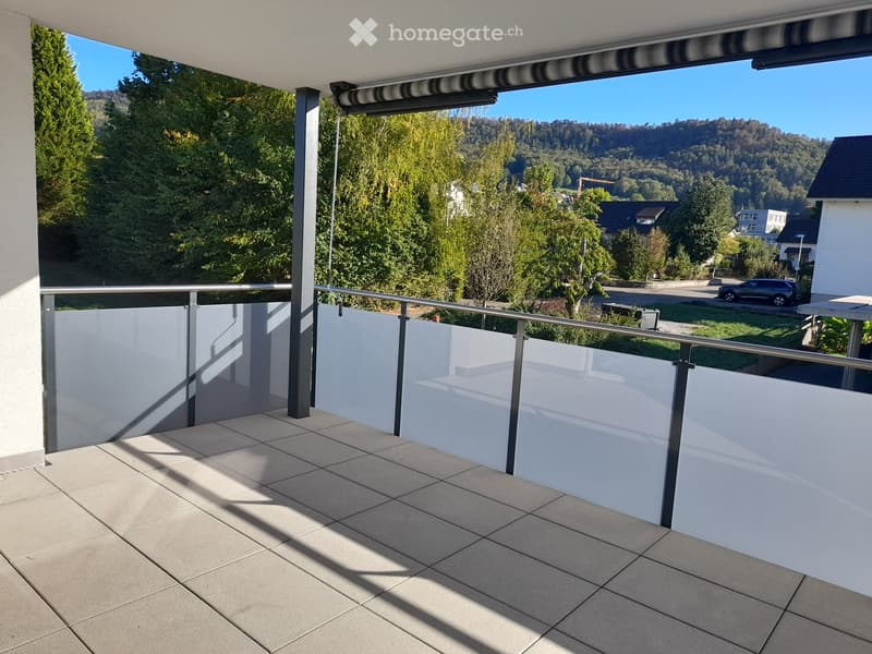 Balcony with tiled floor, white glass balustrade, and scenic view of trees and hills.