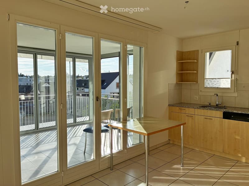 Bright kitchen with large sliding glass doors leading to a balcony, equipped with a table, chairs, sink, and cabinets.