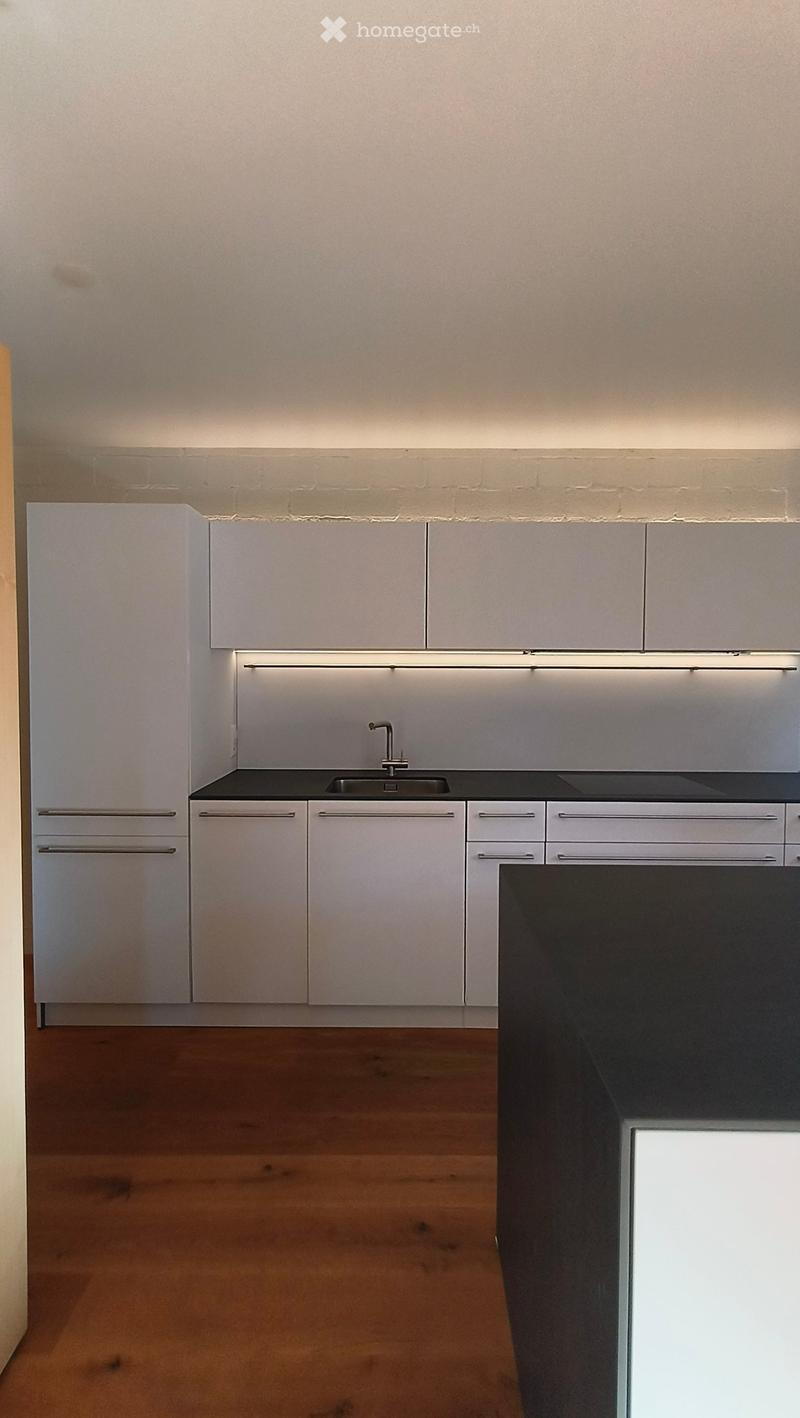 Modern kitchen with white cabinets, dark countertops, and a wooden floor. Features a sink with a modern faucet and built-in lighting above the counter.