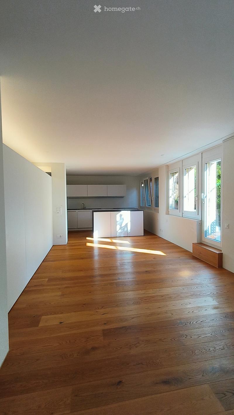 Empty room with wooden flooring, white walls, and large windows allowing natural light to enter. The space is clean and minimalistic with no furniture or decorations.