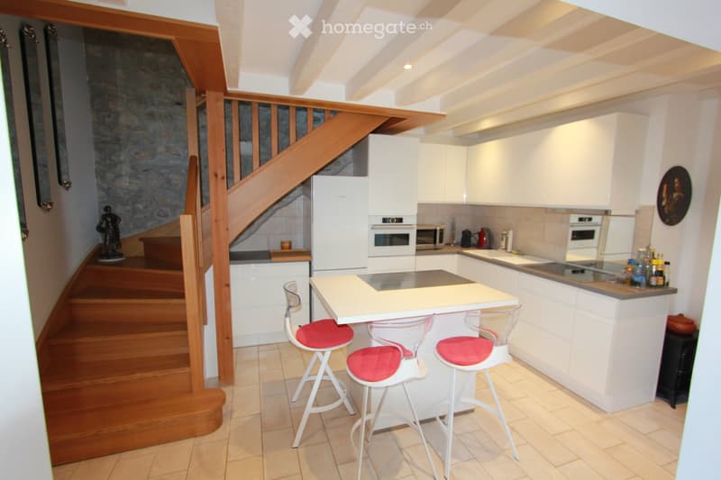 Modern kitchen with white cabinets, stainless steel appliances, a central island with bar stools, and a staircase leading to an upper level.