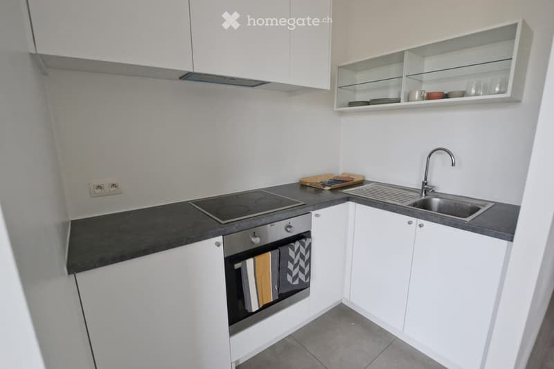 Modern kitchen with white cabinets, stainless steel appliances, and a black countertop. Features an electric stovetop, sink with faucet, and open shelving with dishes and cups.