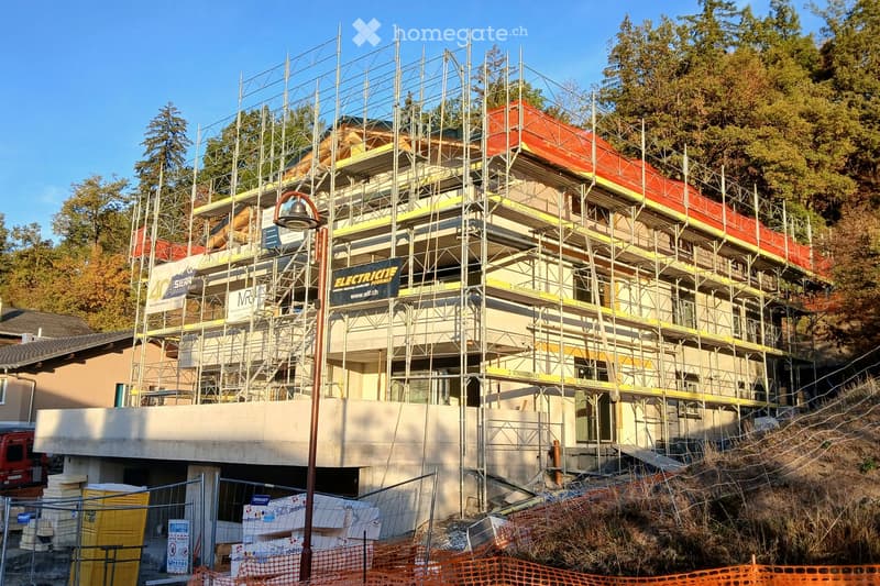 Multi-story building under construction with scaffolding, visible signage, and construction materials around the base.