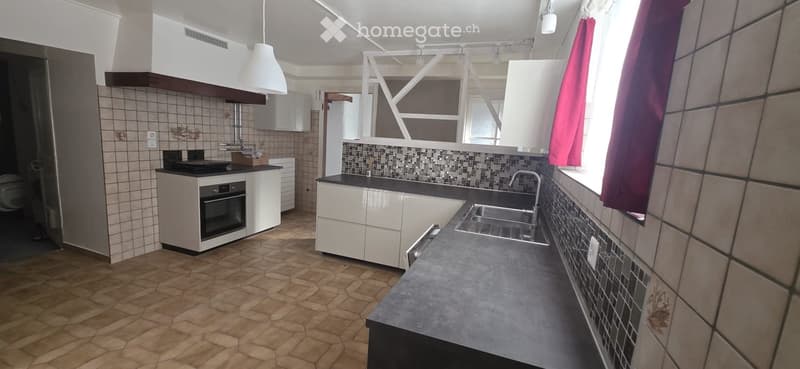 Modern kitchen with white cabinets, dark countertop, stainless steel sink, and built-in oven. Features hexagonal tile flooring and a window with red curtains.