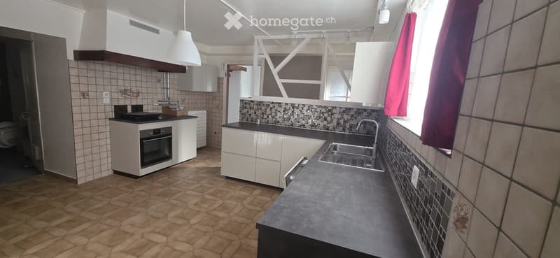 Modern kitchen with white cabinets, dark countertop, stainless steel sink, and built-in oven. Features hexagonal tile flooring and a window with red curtains.