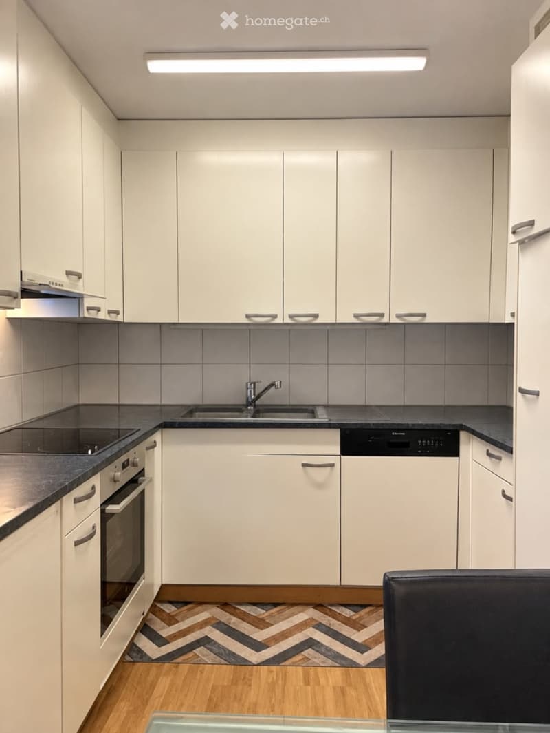 Modern kitchen with white cabinets, black countertops, and a herringbone wooden floor. Features include a sink with a modern faucet, an oven, and a dishwasher.