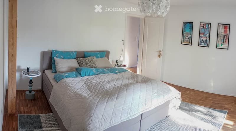 A modern bedroom with a large bed, nightstand, small table, and picture frames on the wall.