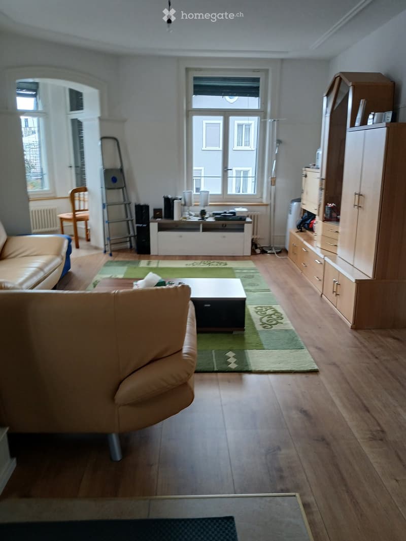 Living room with wooden flooring, two sofas, coffee table, cabinet, and a chair near the window.
