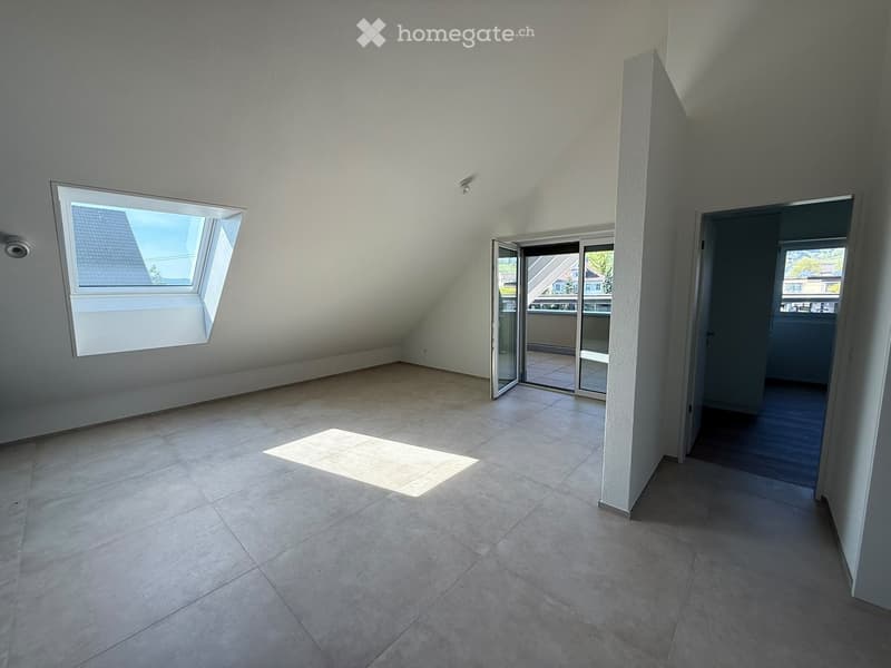 Empty attic room with tiled floor, skylight window, and sliding glass door leading to a balcony.