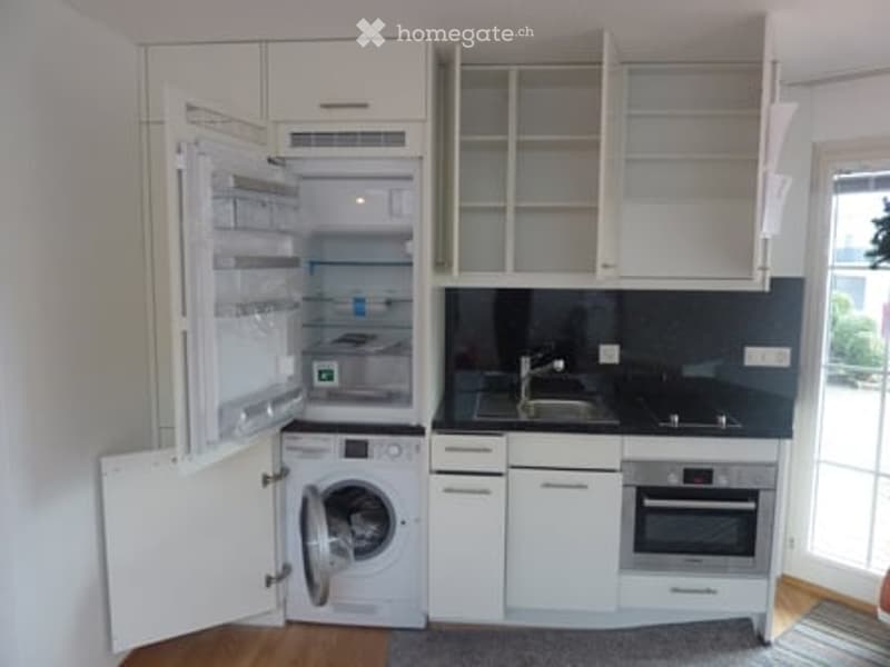 Modern, compact kitchen with white cabinets, stainless steel appliances, and a black countertop.