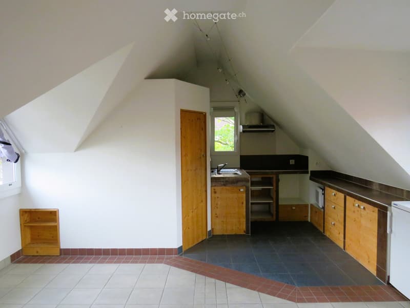 Bright attic kitchen with wooden cabinets, dark countertops, and a sink. Features include a window, shelves, and a refrigerator.