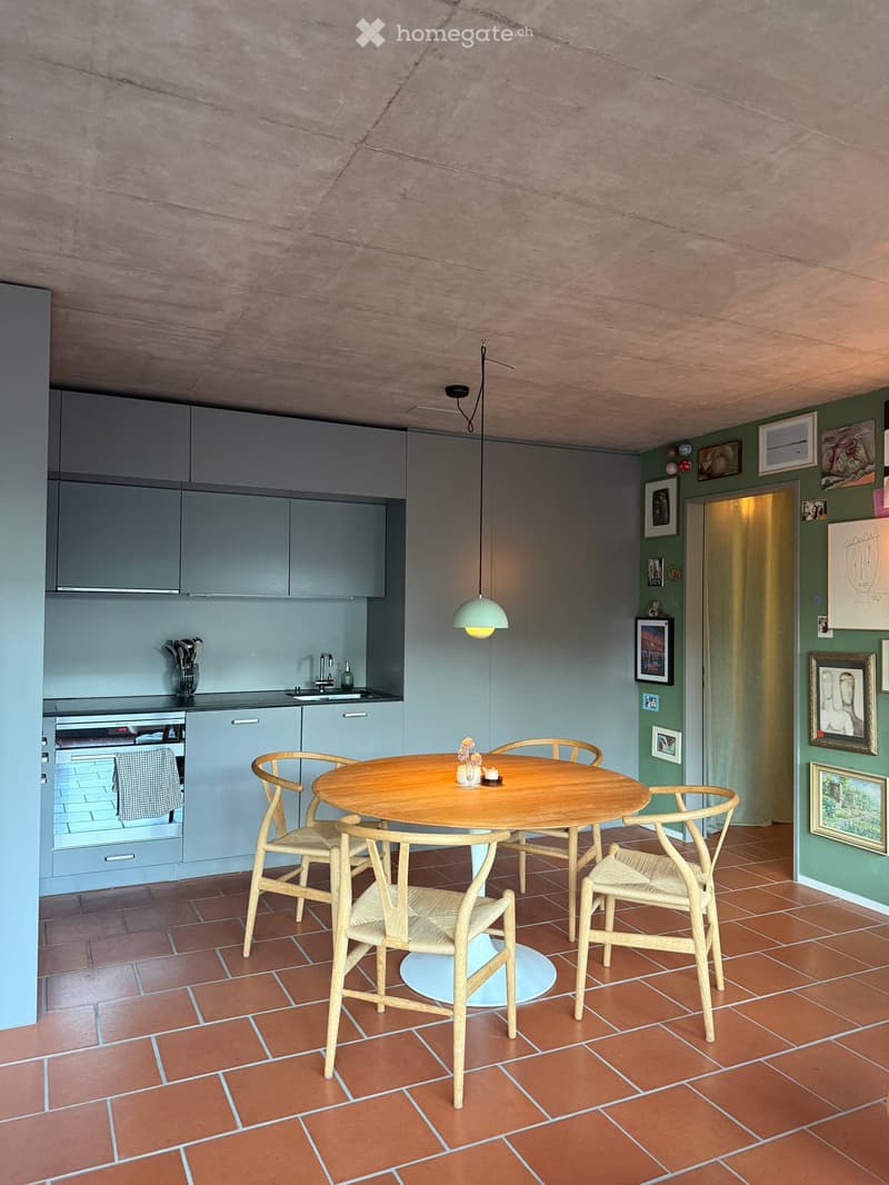 Modern kitchen with grey cabinets, a round wooden dining table with six chairs, a pendant light, and framed pictures on the wall.