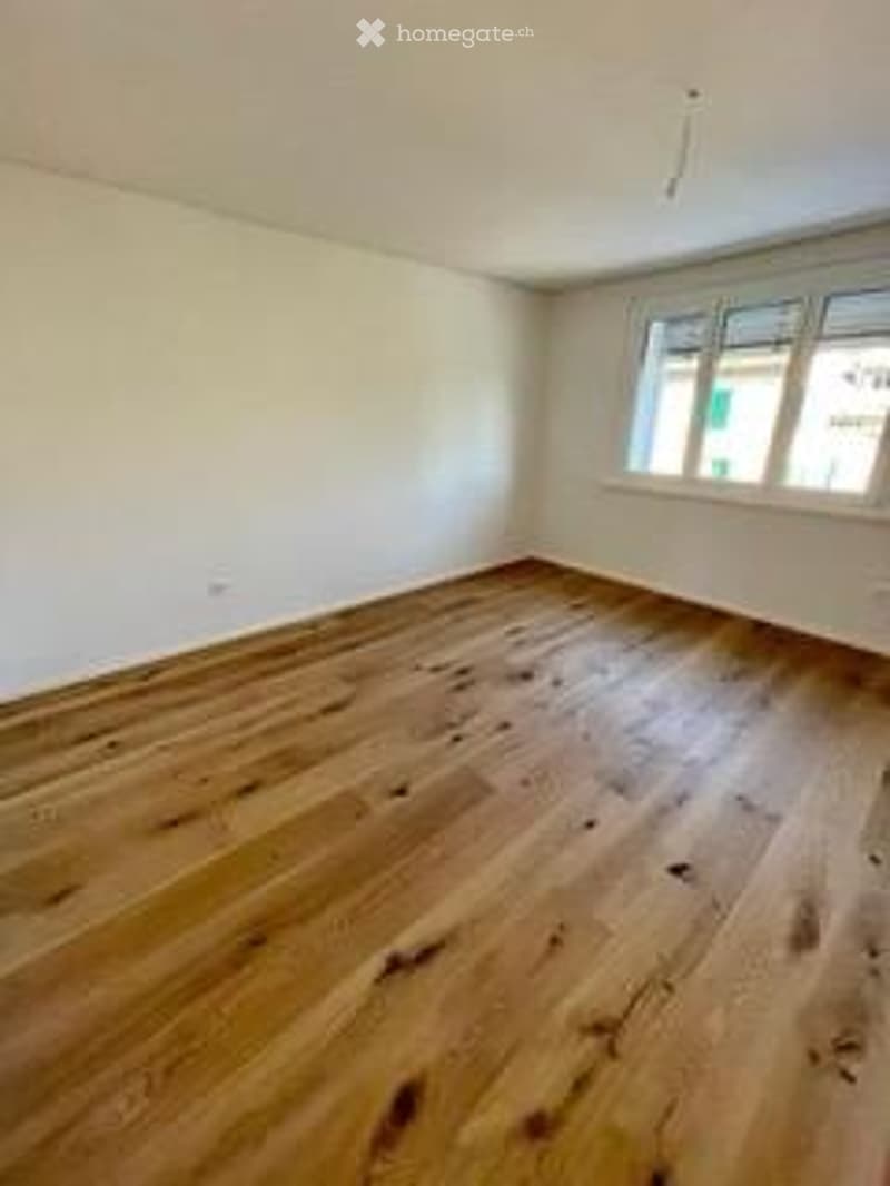 Completely empty room with wooden flooring and large windows, no furniture or equipment.