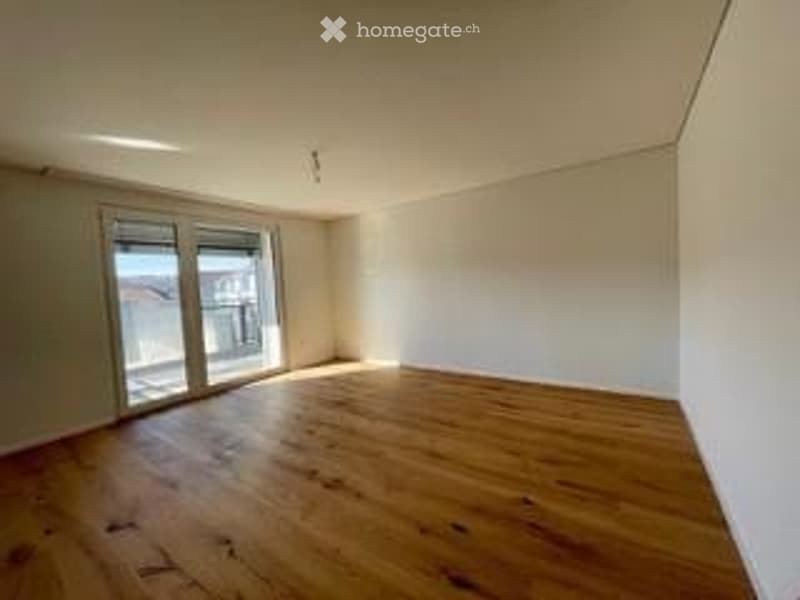 Completely empty room with wooden flooring and large glass doors leading to a balcony or outdoor area.