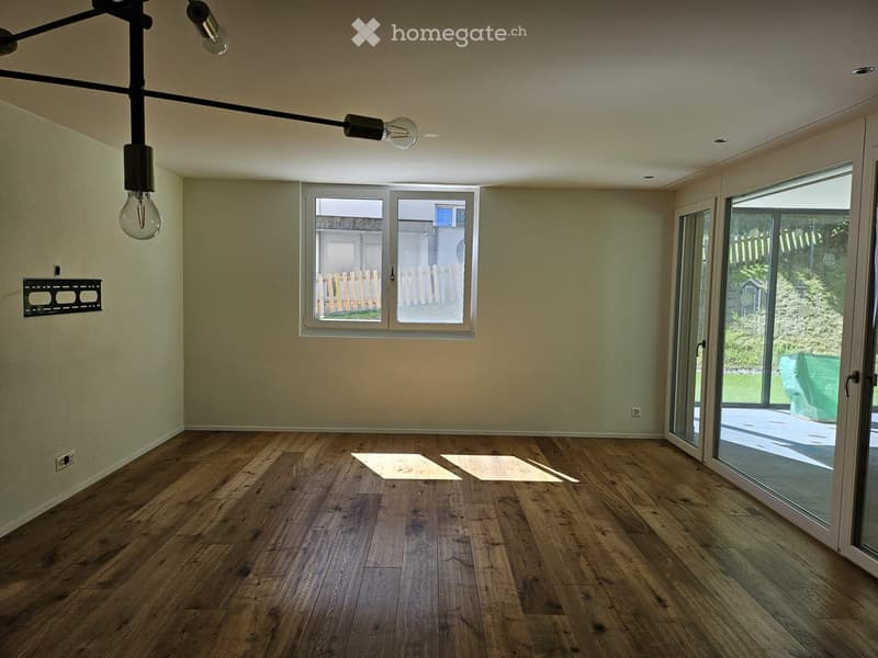 Empty room with wooden flooring, large windows, and a sliding glass door leading to an outdoor area.