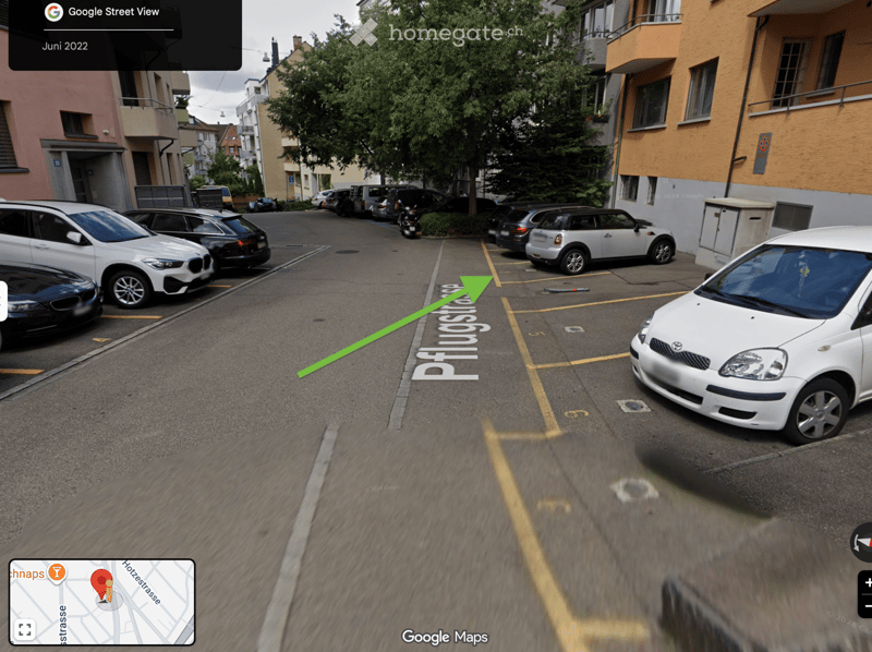 A street view showing a row of parked cars and residential buildings with balconies and windows.