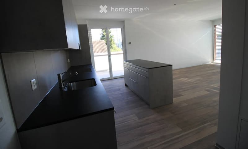 Modern, unfurnished kitchen with dark countertops, built-in cabinets, and a central island. Large sliding glass door leads to a balcony.