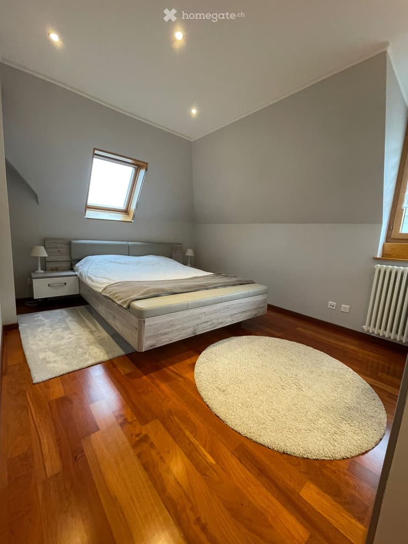 Modern bedroom with wooden flooring, a large bed with a headboard, nightstand with lamp, and two rugs.