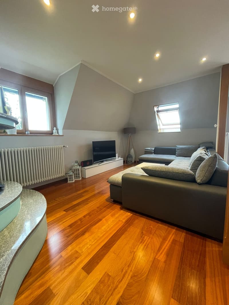 Modern living room with wooden flooring, grey sectional sofa, coffee table, television, floor lamp, radiator, and decorative shelves.