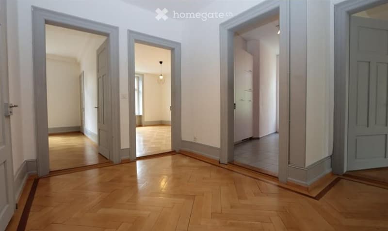 Empty hallway with wooden flooring, multiple open doors leading to other rooms, and neutral-colored walls.