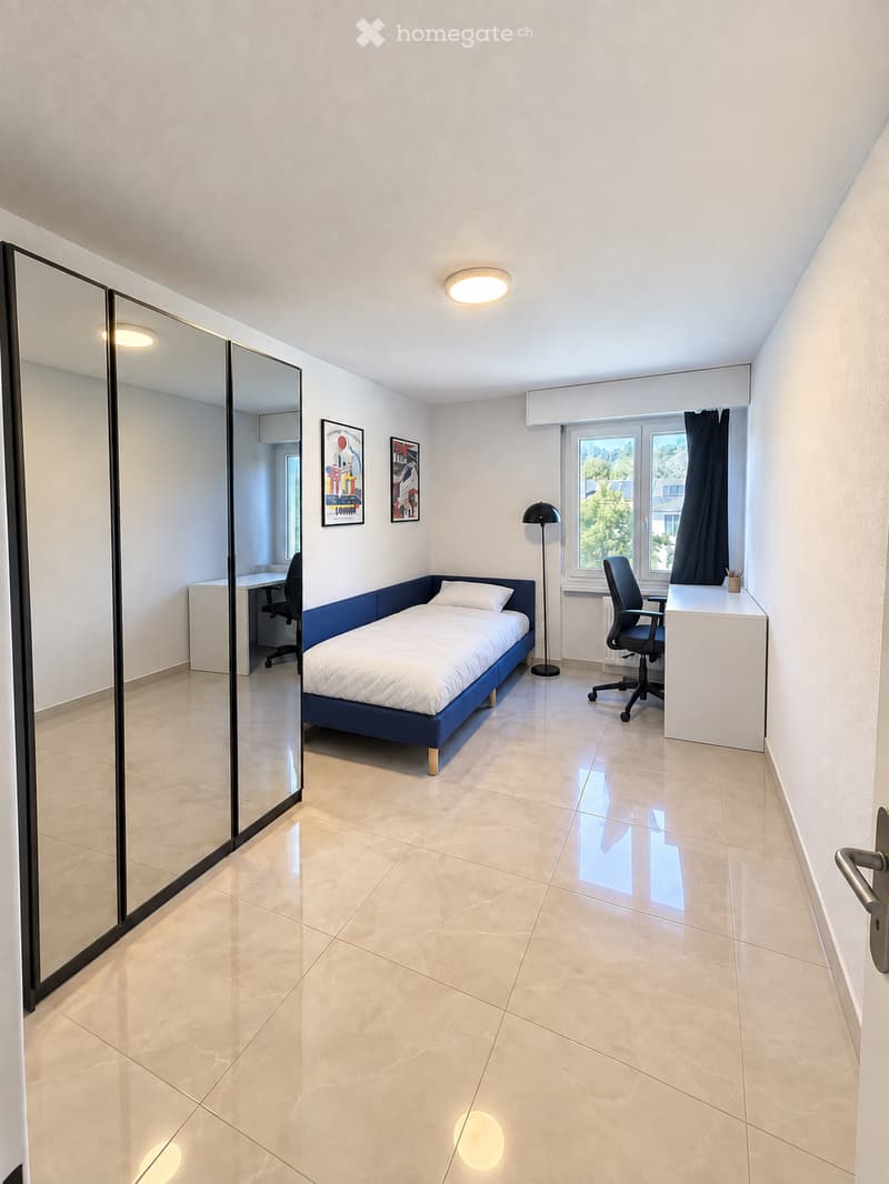Modern, furnished bedroom with a single bed, desk, chair, mirror, and artwork on the wall.