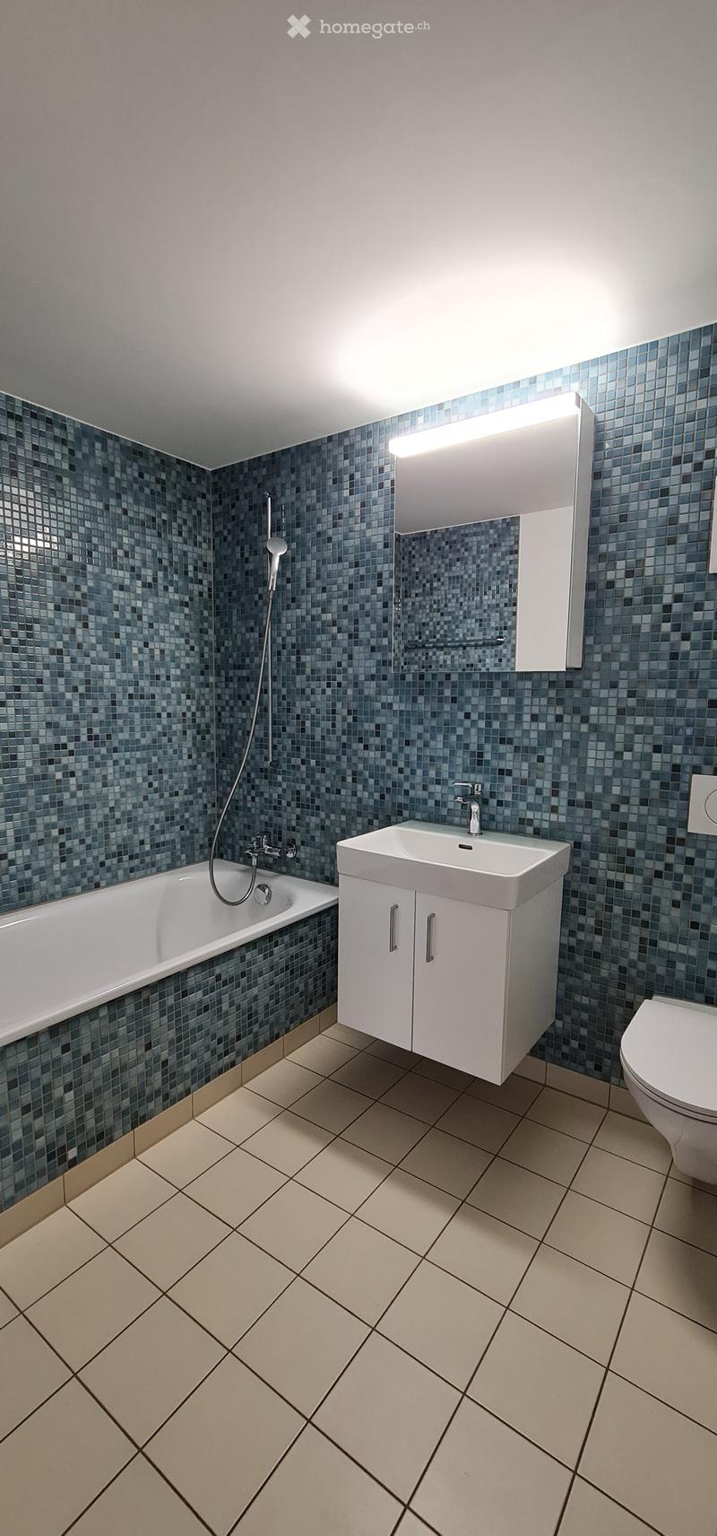 Modern bathroom with blue mosaic tiles, white bathtub, sink, toilet, and built-in cabinet with mirror.