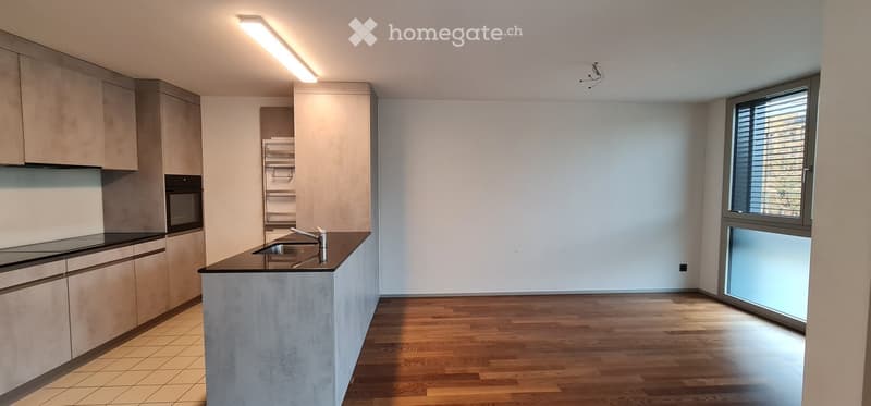 Modern kitchen with light-colored cabinets, a central island with a sink and faucet, and wooden flooring.
